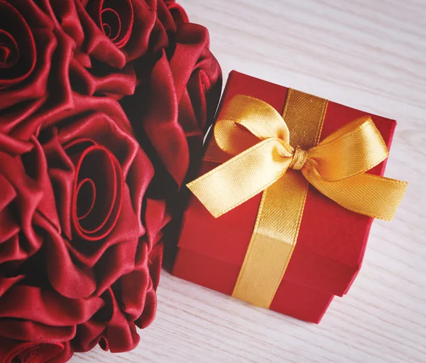 Красные цветы и подарочная коробка с желтой лентой — стоковое фото