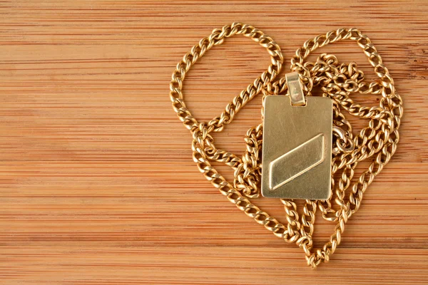 Golden chain  with a rectangular pendant on bamboo wooden background — Stock Photo, Image