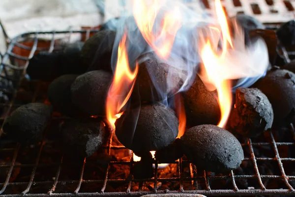 Round charcoal briquettes for barbecue on gril, fire started, flames and smoke break through between the coal briquettes, horizontal orientation