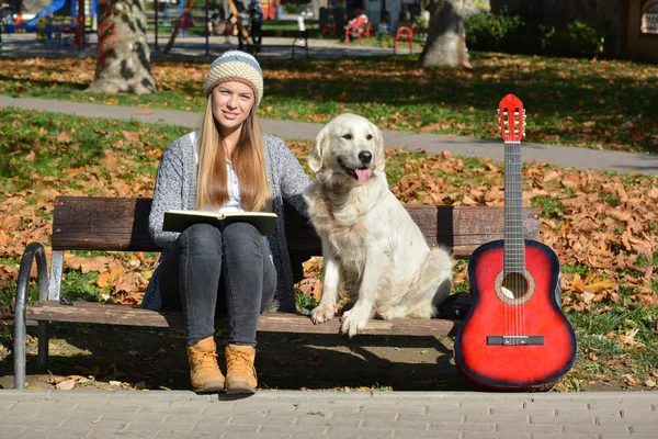Menina, cachorro, livro e guitarra em um banco — Fotografia de Stock