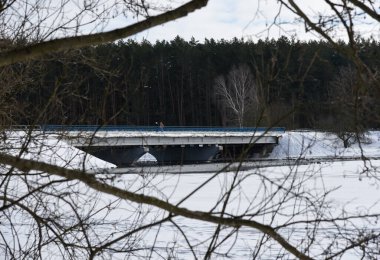İnsanlar kışın donmuş bir nehrin üzerinde uzun bir köprü boyunca yürür..