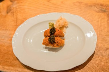 Gourmet sushi dish showcases fresh sea urchin topped with caviar, garnished with wasabi and pickled ginger, presented on a stylish white plate.