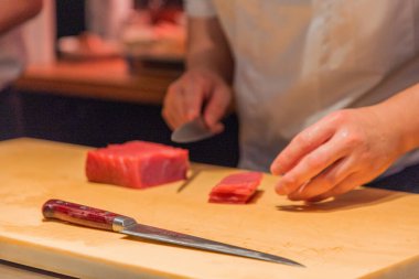 Şef, ahşap kesme tahtasındaki taze ton balığını ustalıkla dilimliyor, canlı bir mutfak ortamında aşçılık uzmanlığı ve hassasiyeti sergiliyor..