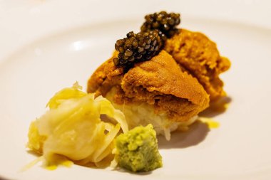 Gourmet sushi dish showcases fresh sea urchin topped with caviar, accompanied by wasabi and pickled vegetables, highlighting culinary artistry.