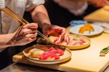 Suşi şefi usta bir şekilde ahşap tabakta canlı suşi parçaları düzenliyor, mutfak sanatını ve detaylara dikkat çekiyor..