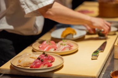 Suşi şefi ahşap tezgahta ustalıkla taze suşi hazırlıyor, canlı renkler sergiliyor ve karışık yemekler sunuyor..