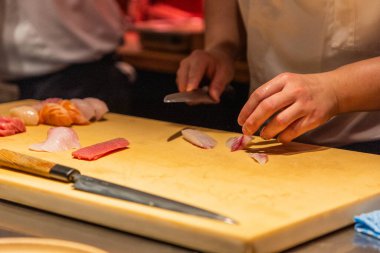 Suşi şefi ahşap kesim tahtasında taze deniz ürünlerini ustalıkla hazırlar. Mutfak uzmanlığı ve canlı renkler sunar..