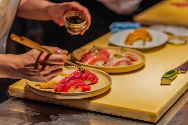 Suşi şefi, ahşap bir tezgahta ustalıkla canlı suşi hazırlıyor. Mutfak sanatını ve detaylara dikkat çekiyor..