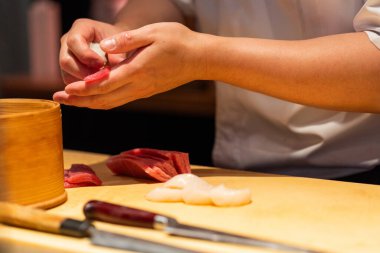 Yetenekli şef, ahşap bir yüzeyde canlı malzemelerle taze suşi hazırlıyor. Mutfak sanatını ve detaylara dikkat çekiyor..