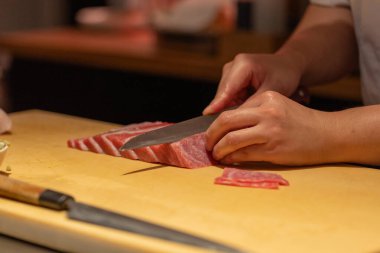 Yetenekli bir şef, ahşap kesim tahtasıyla taze balığı ustalıkla dilimliyor. Mutfak teknikleri ve malzemelerin canlı renklerini sergiliyor..