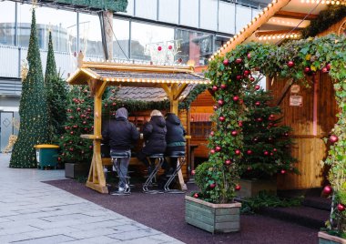 Berlin, Almanya - 01 Ocak 2024: İnsanlar bir Noel pazarında açık ahşap tezgahlarda festival dekorasyonlarıyla oturuyorlar.