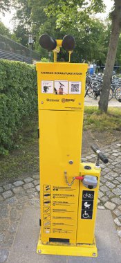 Belin, Almanya - 30 Mayıs 2025: Bisiklet tamir istasyonu canlı bir şehir parkı ortamında araçlar ve talimatlar sunuyor. Hastane