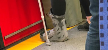 Yürüme botu giyen, baston kullanan, toplu taşıma ortamında duran, taşınabilirlik yardımı ve şehir yaşamını gösteren bir birey.