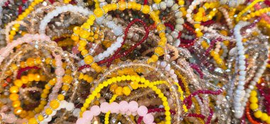 Renkli boncuklu bilezikler sanatsal bir ekrana yerleştiriliyor, çeşitli doku ve renkler sergileniyor, canlı ve göz alıcı bir sahne yaratıyor..