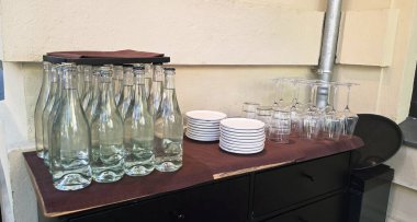 Su dolu cam şişeler, tabakların ve bardakların yanında düzgünce istiflenir, bir olay için davetkar bir atmosfer yaratır ya da toplanır..