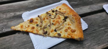 Mantarla kaplanmış gurme pizza dilimi, beyaz bir kağıt tabağa yerleştirilmiş, kırsal ahşap bir masada dinleniyor, iştah açıcı dokular ve renkler sergiliyor..