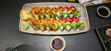 Renkli suşi tabağı, karanlık bir yüzeyde servis edilen, mutfak sanatını ve canlı sunumunu sunan bir dizi süslemeli rulo içeriyor..