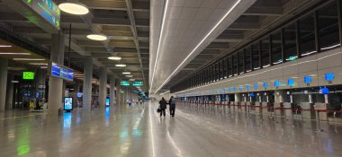 Doloman, Türkiye - 25 Nisan 2025: Modern havaalanı terminalinde gezginler parlak ışıklandırmayla geniş salonda yürüyorlar.