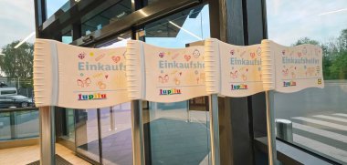 Belin, Almanya - 19 Mayıs 2025: Alışveriş merkezi girişinde Einkaufen tabelaları ve modern mimari ile renkli bayraklar yer alıyor.