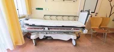 Berlin, Almanya - 16 Haziran 2025: Hastane odasında tıbbi teçhizatlı ve sandalyeli boş bir hasta yatağı.