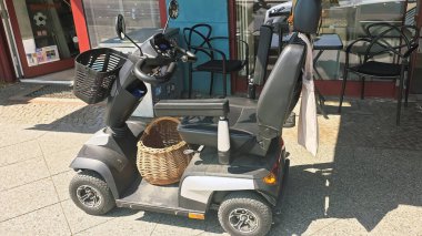 Berlin, Almanya - 17 Haziran 2025: Mobilite scooter bir kafe önünde park halinde, alışveriş kolaylığı için bir sepet sunuluyor.