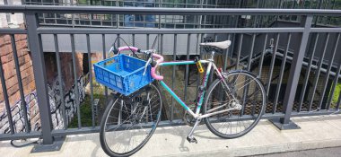 Berlin, Almanya - 3 Temmuz 2025: Mavi sepetli renkli bisiklet, arkasında grafiti olan şehir köprüsünde park halinde.