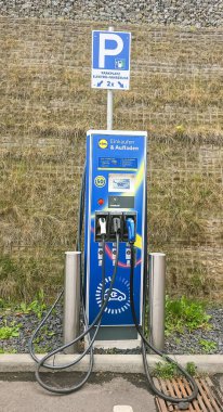 Berlin, Almanya - 07 Haziran 2025: Çevrede yeşil ile çevrili park levhası bulunan elektrikli araç şarj istasyonu.
