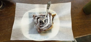Üzerinde pudra şekeri olan lezzetli bir çikolatalı pasta, parşömen kağıdına konmuş, kırsal ahşap bir masada dinleniyor, davetkar ve iştah açıcı..
