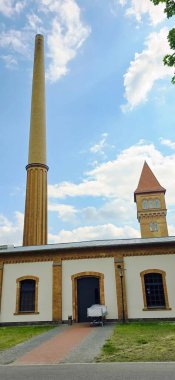 Belin, Almanya - 30 Mayıs 2025: Tarihi endüstriyel yapı açık mavi gökyüzünün altında uzun bir baca ve saat kulesine sahiptir. Hastane