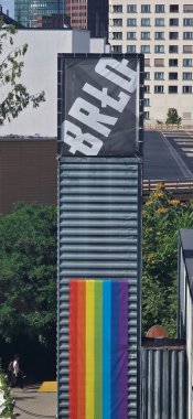 Berlin, Almanya - 4 Temmuz 2025: BRLD işareti yeşillik dolu bir şehir manzarasında canlı bir gökkuşağı bayrağı ile dimdik ayakta duruyor.