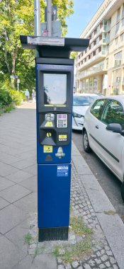 Berlin, Almanya - 07 Ağustos 2025: Otoparkmetre şehir caddesinde duruyor ve yakınındaki binalar park halinde.