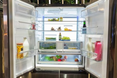 . Modern buzdolabında sağlıklı yaşam için çeşitli meyve, sebze ve içecekler sergilenen taze yiyecek öğeleriyle dolu raflar yer alıyor.