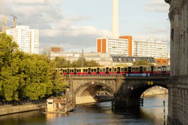 Berlin, Almanya - 17 Haziran 2025: Berlin tramvayı nehir üzerinden canlı şehir silueti ile köprüyü geçiyor.