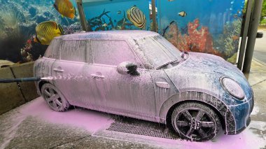 Berlin, Germany - May 18, 2025: Mini Cooper is being washed with foam at a car wash featuring an underwater mural.