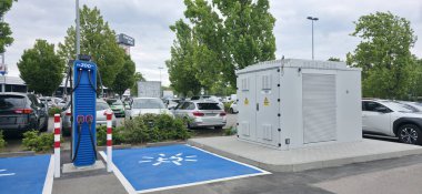 Berlin, Germany - June 28, 2025: Electric vehicle charging station features power unit in busy parking lot surrounded by trees.