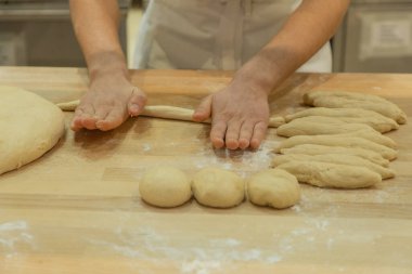 Baker's hands skillfully rolling dough on a wooden surface, surrounded by flour and shaped pieces, showcasing culinary expertise.