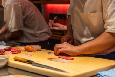 Skilled chef is preparing sushi with fresh ingredients on a wooden cutting board, showcasing culinary expertise and vibrant colors of fish.