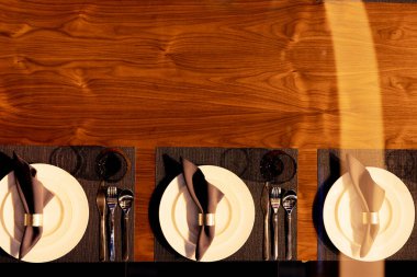 . Zarif yemek masası tabakları, çatal bıçakları ve ahşap bir yüzeye yerleştirilmiş peçeteleri içerir. Sofistike bir atmosfer yaratırlar.