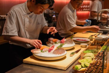 Berlin, Germany - August 19, 2025: A skilled Asian sushi chef meticulously arranges fresh sashimi on ice in a modern restaurant kitchen, showcasing culinary artistry and attention to detail.