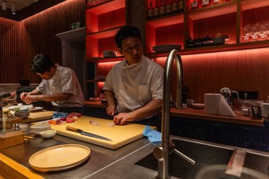 Berlin, Germany - August 19, 2025: Two Asian male sushi chefs skillfully prepare fresh seafood in a contemporary kitchen, showcasing their culinary expertise vibrant atmosphere restaurant.