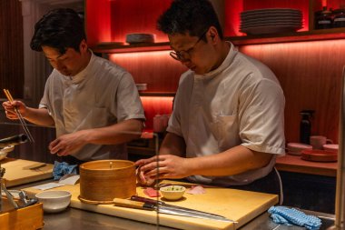 Berlin, Germany - August 19, 2025: Two asian male sushi chefs skillfully prepare fresh fish contemporary kitchen, showcasing their culinary expertise and attention detail in a vibrant atmosphere.