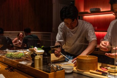 Berlin, Germany - August 19, 2025: A skilled Asian chef is meticulously preparing sushi at a modern restaurant, showcasing fresh ingredients and vibrant decor, creating an inviting dining atmosphere.