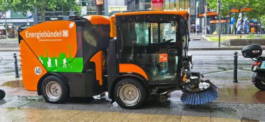 Berlin, Germany - July 17, 2025: . Compact street sweeper vehicle is cleaning urban area with vibrant branding and wet pavement