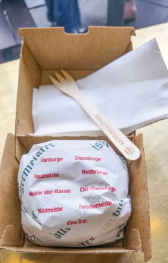 Berlin, Germany - September 05, 2025: . Gourmet burger wrapped in paper, placed inside takeout box with wooden fork and napkin