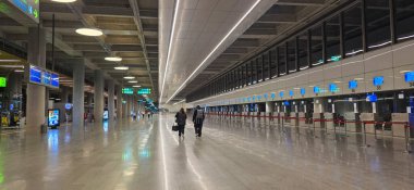 Doloman, Turkey - April 25, 2025: Modern airport terminal features travelers walking towards check-in counters with bright lighting.