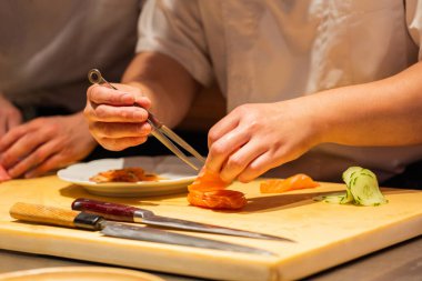 Yetenekli şef, ahşap kesim tahtasında taze malzemeler kullanarak suşi hazırlıyor. Mutfak teknikleri ve canlı renkler sergiliyor..