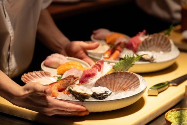 Enfes suşi tabağı bir şef tarafından servis ediliyor, taze deniz ürünleri, garnitürler ve buz sergileniyor, canlı bir mutfak deneyimi yaratıyor..