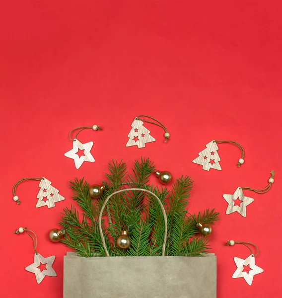 クリスマスの構成 コピースペース クリスマスツリーの枝や赤い背景に木製のおもちゃとエコペーパーバッグ クリスマスの到来と贈り物の配達の概念 — ストック写真