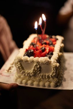Koyu arkaplanda doğum günü pastası ve mumlar.