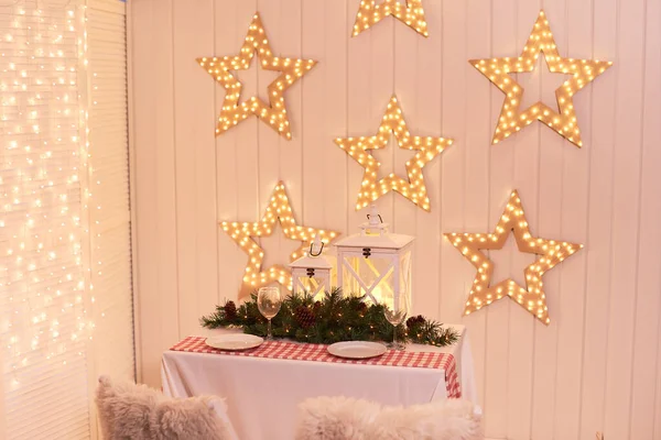 Dining room decorated for Christmas. Table with chairs set, waiting for guests. The wall is decorated with luminous stars, Xmas Home Interior. Traditionally decorated christmas table